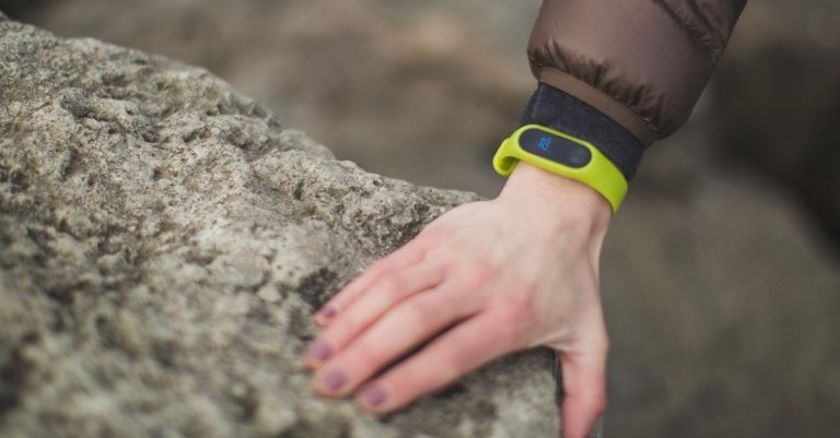 Close-up of a hand with a fitness tracker touching a rock outdoors, showcasing exploration.