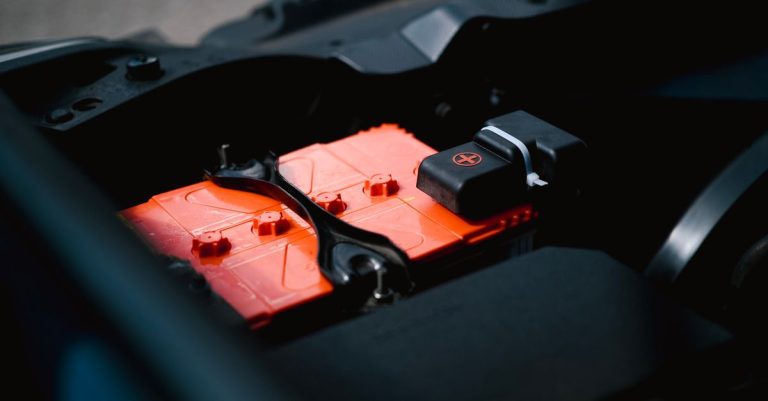 Detailed view of an orange car battery inside a vehicle's engine bay, highlighting its features.