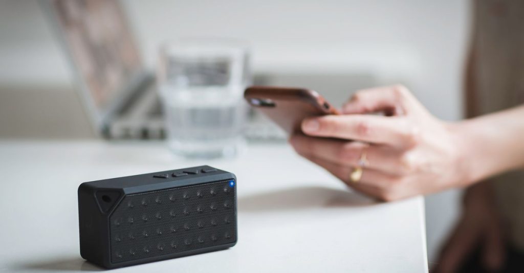 Person connecting a smartphone to a wireless speaker indoors, foreground focus.