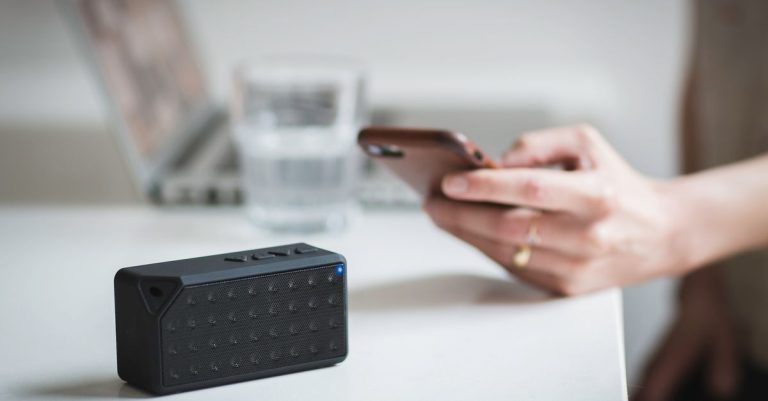 Person connecting a smartphone to a wireless speaker indoors, foreground focus.