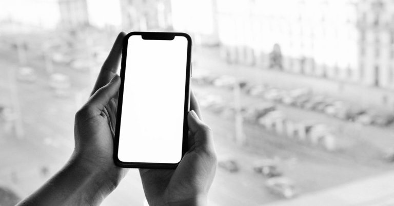 Black and white image of hands holding a smartphone with a blank screen, outdoor city view.