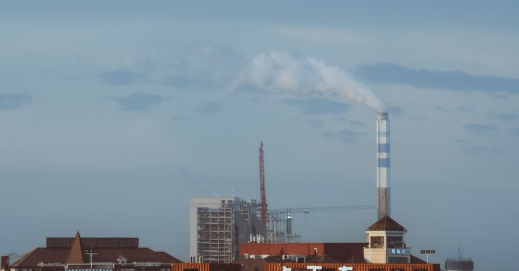 Factory with smokestack emitting smoke under a clear sky, industrial setting.