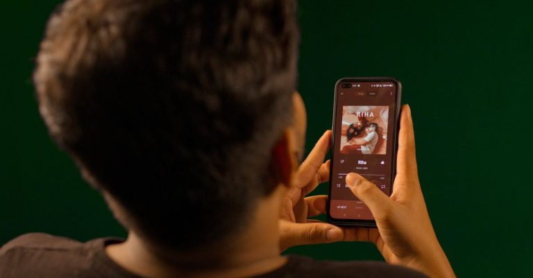 A person using a smartphone to stream music from a streaming service app indoors.