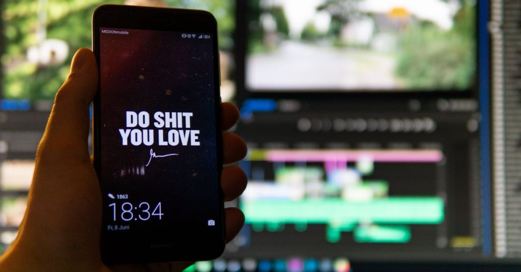 Close-up of a smartphone displaying an inspirational message against a video editing background.