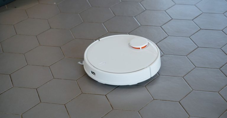 A sleek, white robotic vacuum cleaner operating on a hexagonal tiled floor.