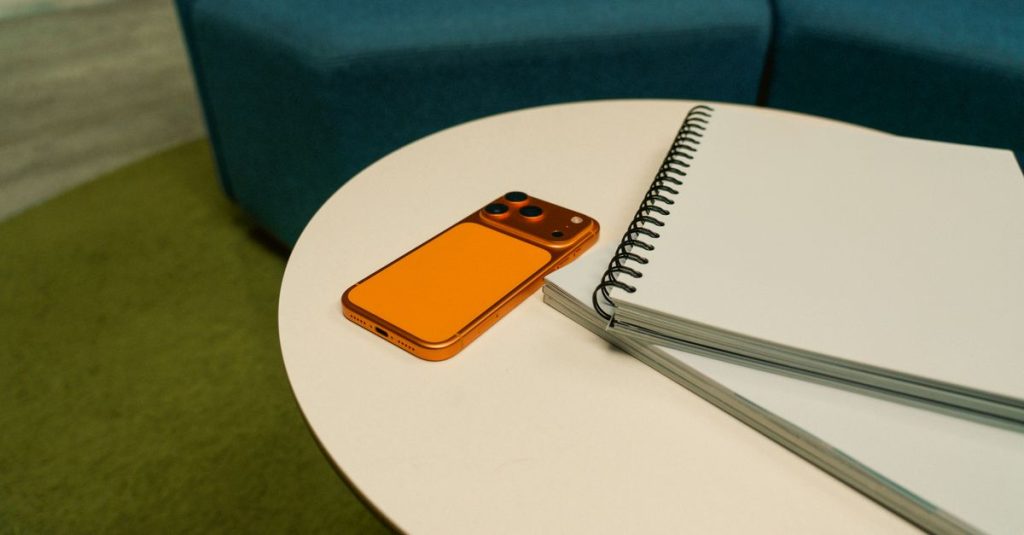 A stylish office setting featuring a spiraled notepad and an orange smartphone on a round table.