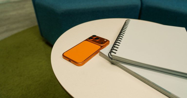 A stylish office setting featuring a spiraled notepad and an orange smartphone on a round table.