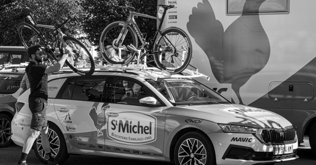 Man securing bicycles on a Skoda support vehicle in an urban setting, perfect for sports event coverage.