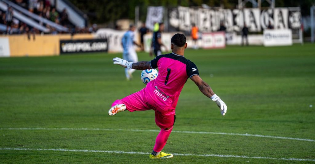 A goalkeeper in bright pink kit kicking a soccer ball during a match.