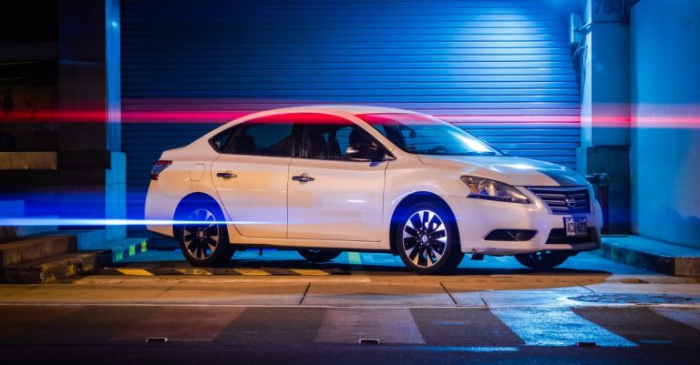A white car parked in an urban setting at night, illuminated by vibrant red and blue light trails.