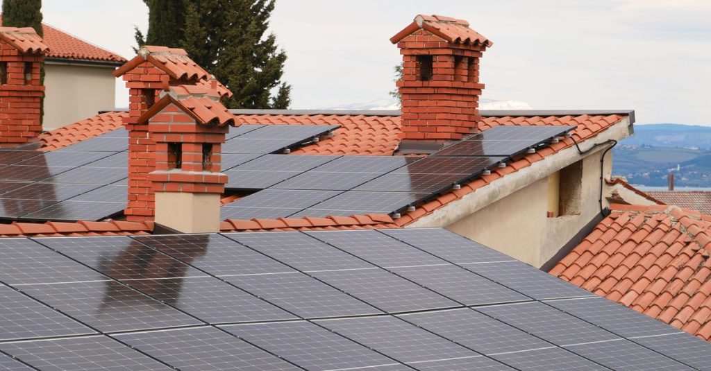 Solar panels on tiled roofs of houses with chimneys, capturing clean energy.