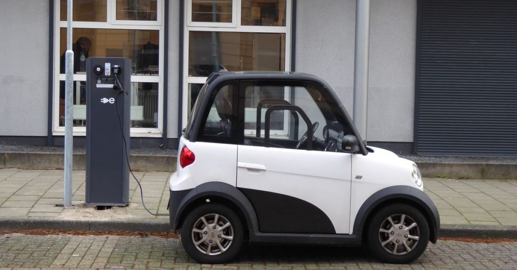 A white and black compact electric car charging at a public power station.