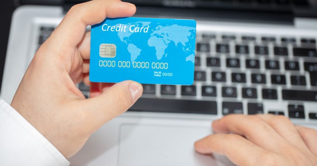 Person holding credit card near laptop for online shopping, emphasizing secure online transactions.