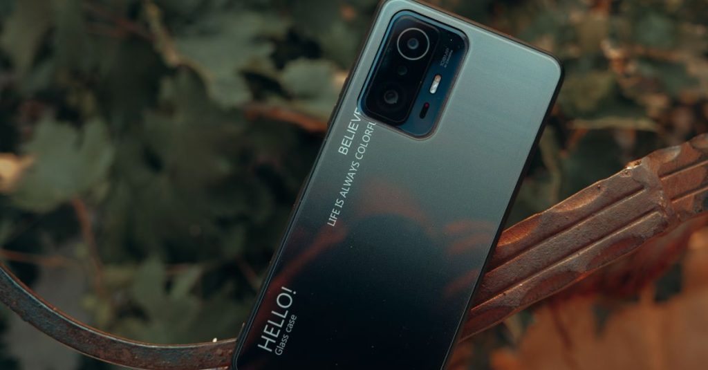A close-up of a smartphone placed outdoors with a nature background, showcasing design details.