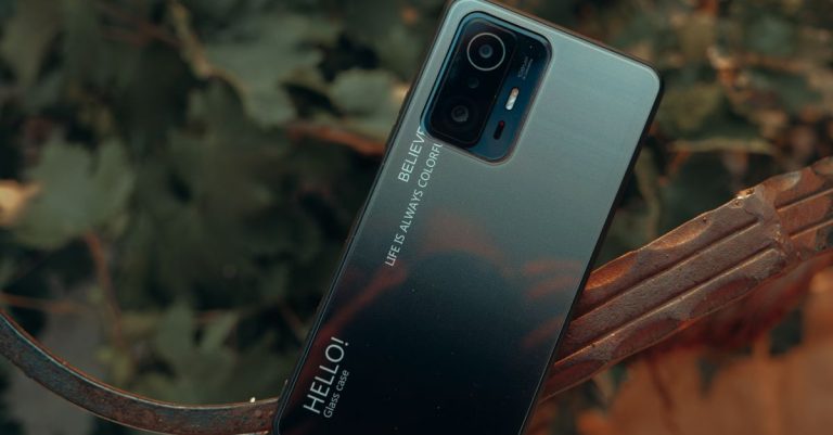 A close-up of a smartphone placed outdoors with a nature background, showcasing design details.