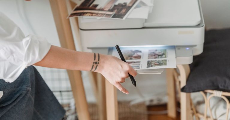 High angle of crop anonymous female photographer using printer for making images while working in flat